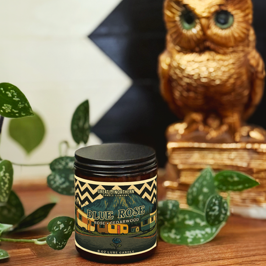 Candle jar labeled 'Blue Rose' with decorative owl and plants in the background