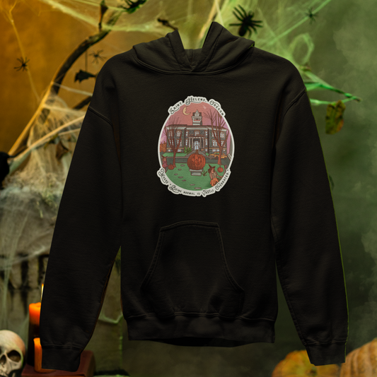 Black hoodie with a haunted house design on the back, set against a Halloween-themed background with pumpkins and candles.